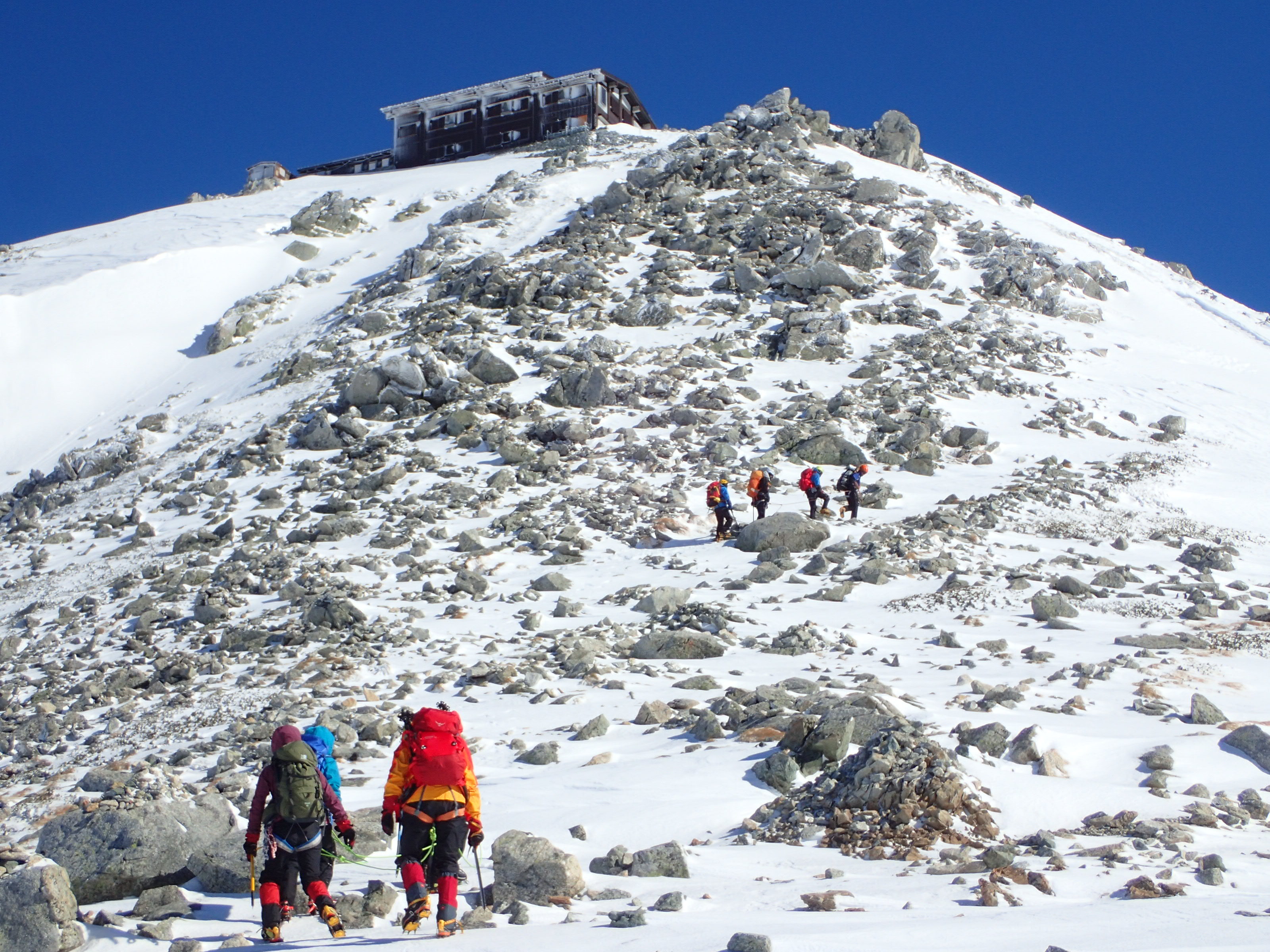 雄山頂上直下の岩と雪の斜面を登る